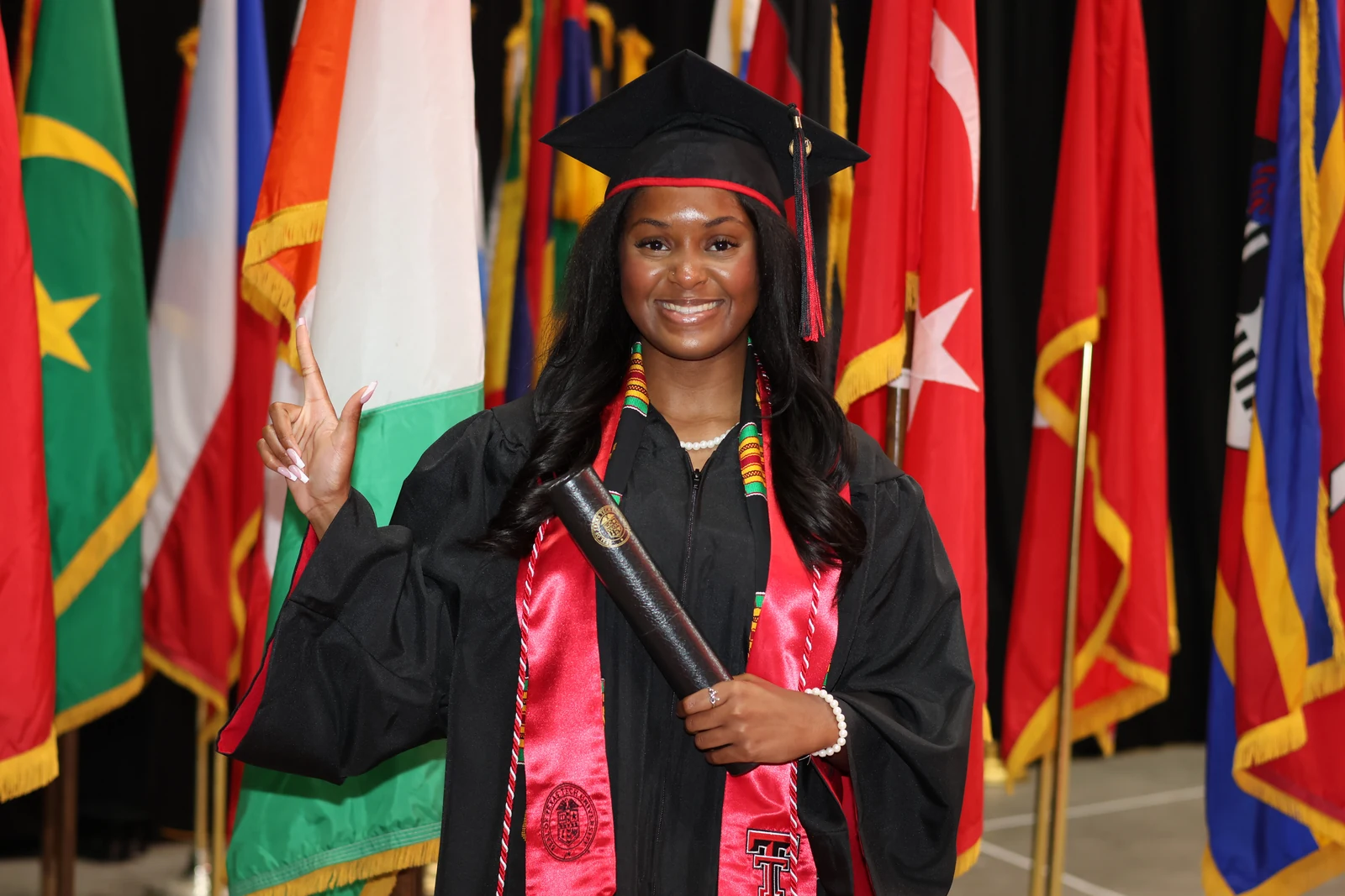 Smiling graduate in a black cap and gown with a red stole